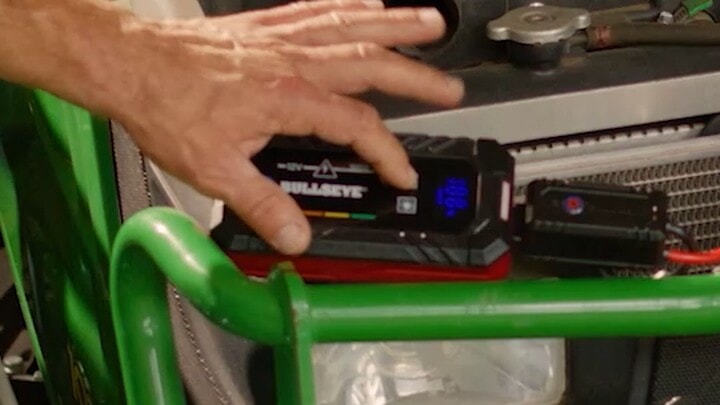 Bullseye Safety XL jump starter on a tractor battery with the operator reaching for it