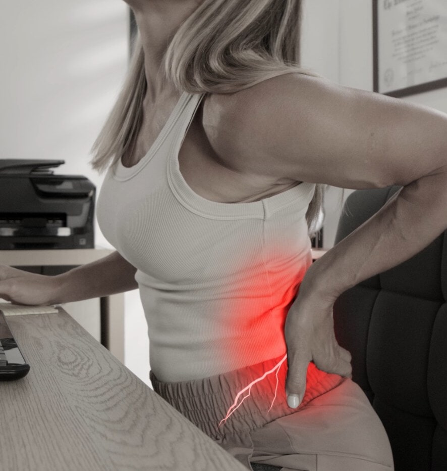 A woman holding her lower back in pain while sitting at her desk